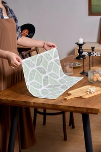 Detail of Nordic style green leaf print linen napkin held by hands over wooden table