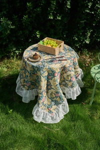 Detail of floral jacquard tablecloth with double-layered white lace ruffles in outdoor setting