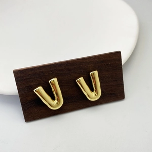 Pair of polished gold-finished V-shaped letter studs on a classic wooden display card