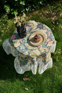 Detail of vintage floral tapestry tablecloth with white lace ruffle edge in outdoor light