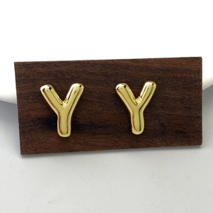 Minimalist polished golden metal letter Y stud earrings on a natural wood stand
