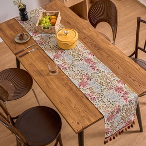 Floral table runner with pink jacquard patterns and elegant dark tassels on a wooden table