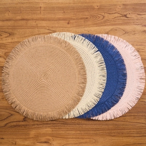 Modern circular woven placemats with fringe in brown, cream, blue, and pink on wood