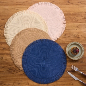 Detailed view of woven round placemats with fringe in pink, beige, tan and blue colors