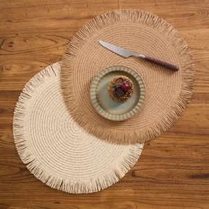 Detail of round woven placemats with tassel edges on a wooden table for home decor