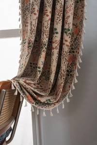 Detail of bohemian floral jacquard curtain with tassels on a vintage wicker chair