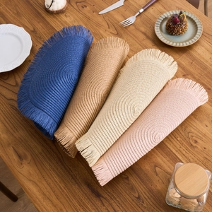 Set of four woven round placemats with fringe edge in blue, brown, beige, and pink