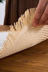 Close-up of flexible beige woven placemat with decorative tassels on wooden table