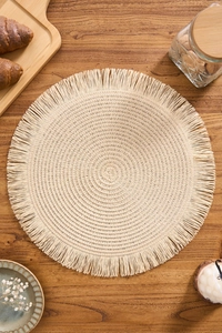 Detail of round woven placemat with tassels on a wooden table with breakfast props