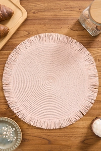 Close-up of pink round woven placemat with delicate fringe detail on a wooden table