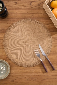 Macro shot of a round woven placemat with delicate fringe on a rustic wooden table