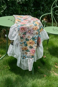 Detailed view of floral jacquard fabric with white multilayer lace edges on a garden table