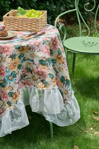 Close-up of floral fabric tablecloth featuring white lace edges in a garden setting