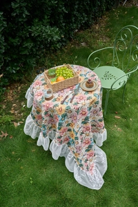 Close-up of jacquard floral tablecloth featuring white lace edges on outdoor garden table