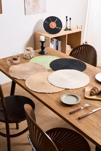 Detail of woven round placemats with scalloped edges in five pastel colors on a wooden table