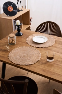 Detail view of woven cotton round placemats with delicate scalloped braid edges on wood