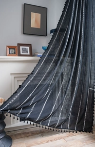 Macro detail of black curtain with white geometric embroidery and hanging tassels