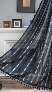 Détail du rideau de style bohème noir avec tissage géométrique blanc et pompons