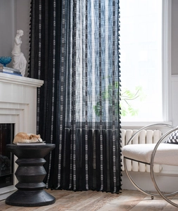 Détail d'un rideau noir semi-transparent avec motifs géométriques blancs et franges