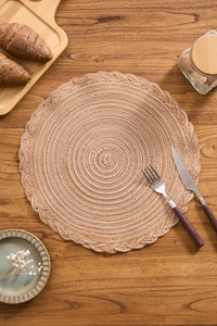 Close-up of a rustic round woven placemat with intricate braided edges on a wood table