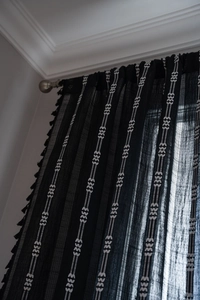 Vue détaillée d'un rideau semi-transparent noir avec broderie blanche et pompons à franges