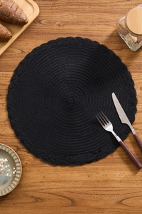Close-up of black braided round placemat with woven lace edges on wooden table