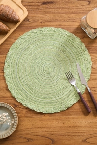 Detail of green woven cotton place mat with braided edges on a wooden table setup
