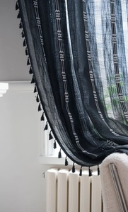 Détail du rideau noir semi-transparent avec broderie blanche et pompons à franges