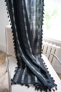 Détail d'un rideau en maille noire avec broderie blanche et franges sur une chaise
