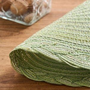 French country style woven cotton table mat with green spiral pattern on wooden desk