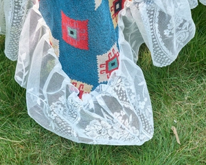 Macro detail of blue geometric jacquard fabric with delicate white lace trim on grass