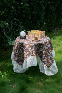 Close-up of vintage floral tablecloth with white wide lace ruffle edges in garden setting