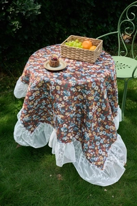 Detail of vintage floral tablecloth with white lace ruffle edge on outdoor round table