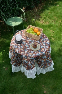 Detailed view of vintage floral tablecloth with white lace ruffle edges on garden table