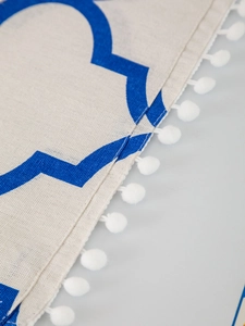 Detail of blue geometric patterns and white pom-pom fringe on a cotton linen dust cover