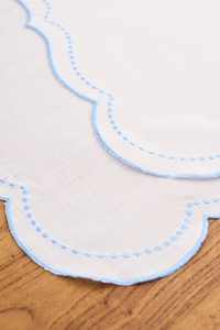 Macro shot of scalloped edges and blue embroidery on white linen napkin fabric