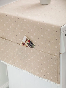 Detail of beige daisy dust cover with storage side pockets and white pom-pom fringe