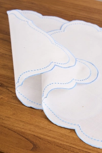 Detail of scalloped light blue embroidered edges on white cotton linen table napkins