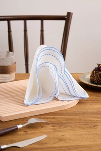 Close-up of white linen napkin with blue scalloped embroidery on a wooden tray