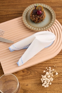 Detail of white linen napkin with blue embroidery folded into bunny ears on a wooden tray