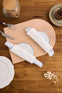 Close-up of white cotton linen napkin with blue embroidery edge on wavy wooden tray