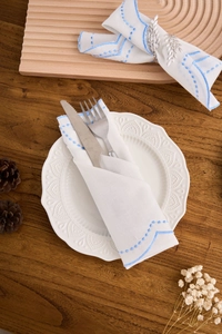 Close-up of white cotton napkin with blue scalloped embroidery and leaf napkin ring