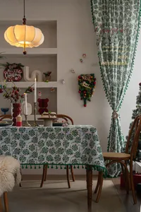Detailed view of green Christmas tablecloth with elegant floral prints and tassel edges