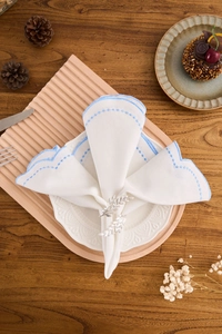 Detail of leaf napkin ring and white linen napkin with blue scalloped embroidery