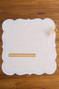 Close-up of white linen napkin with blue wave embroidery and dots on wooden table