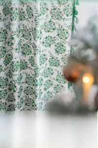 Close-up of green holly leaf pattern on white fabric with elegant green tassels