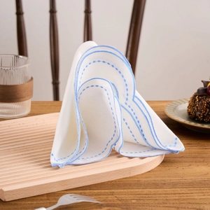 Elegant white cotton linen napkin with blue embroidery on wavy wooden tray