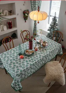 Detailed view of rectangular Christmas tablecloth with green floral prints and pom-pom tassels