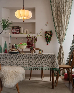 Detail of holly leaf tablecloth featuring dark green pom pom fringe for Christmas decor