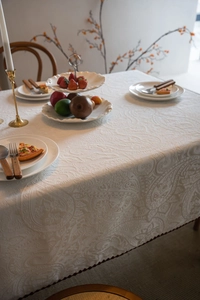 Detailed macro view of cream paisley jacquard tablecloth with refined burgundy piping edge